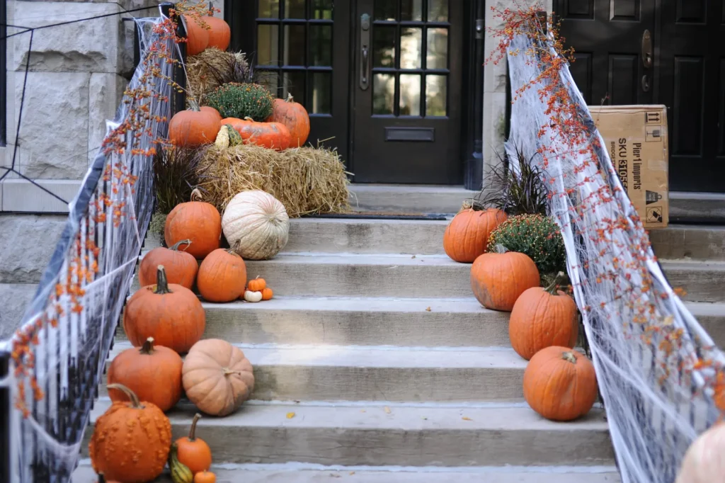 Stairs with pumpkins, gourds, orange flowers, a hay bale, and cobwebs.